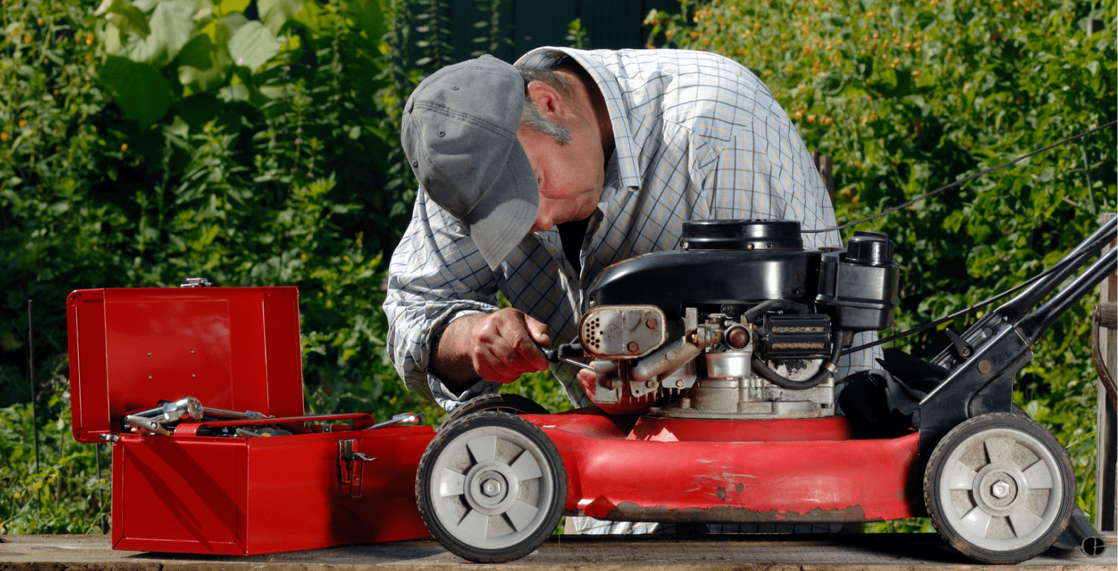 Man repairing lawnmower with red toolbox nearby.