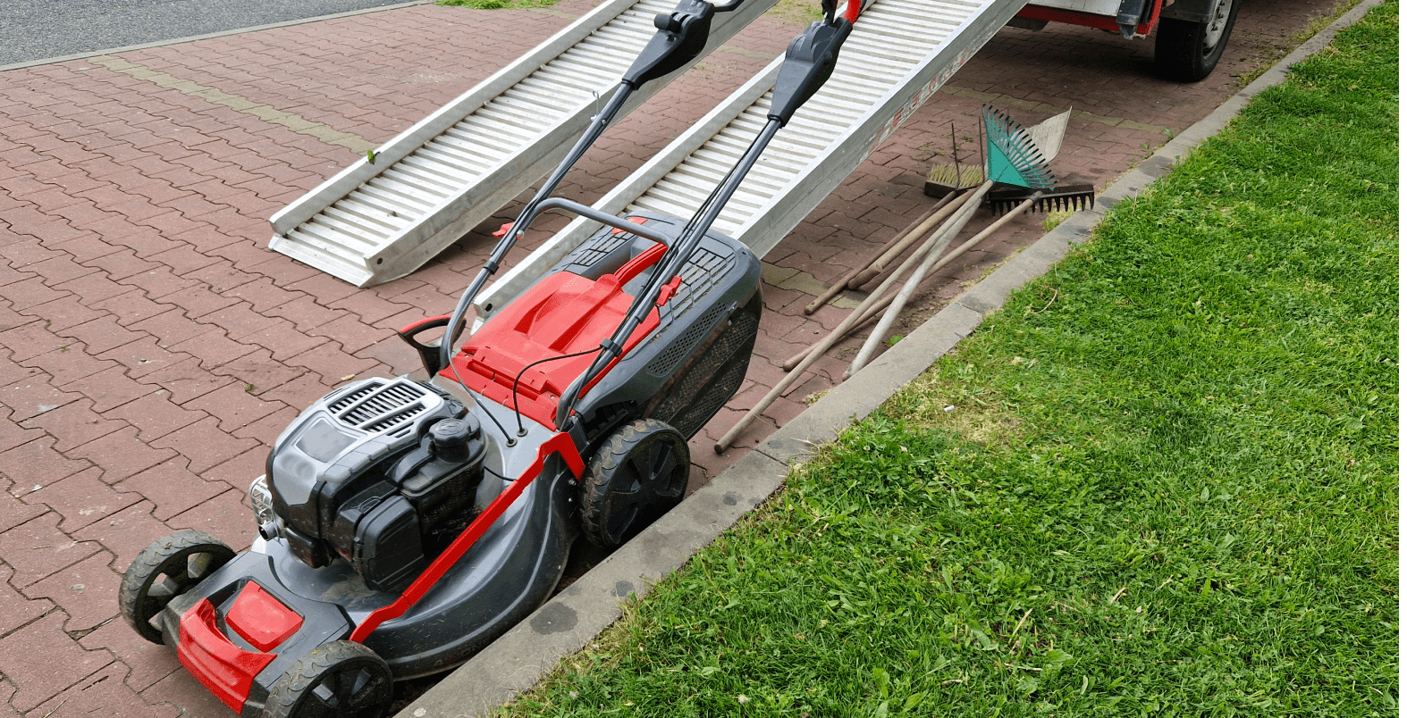 Lawnmower near ramp with gardening tools.