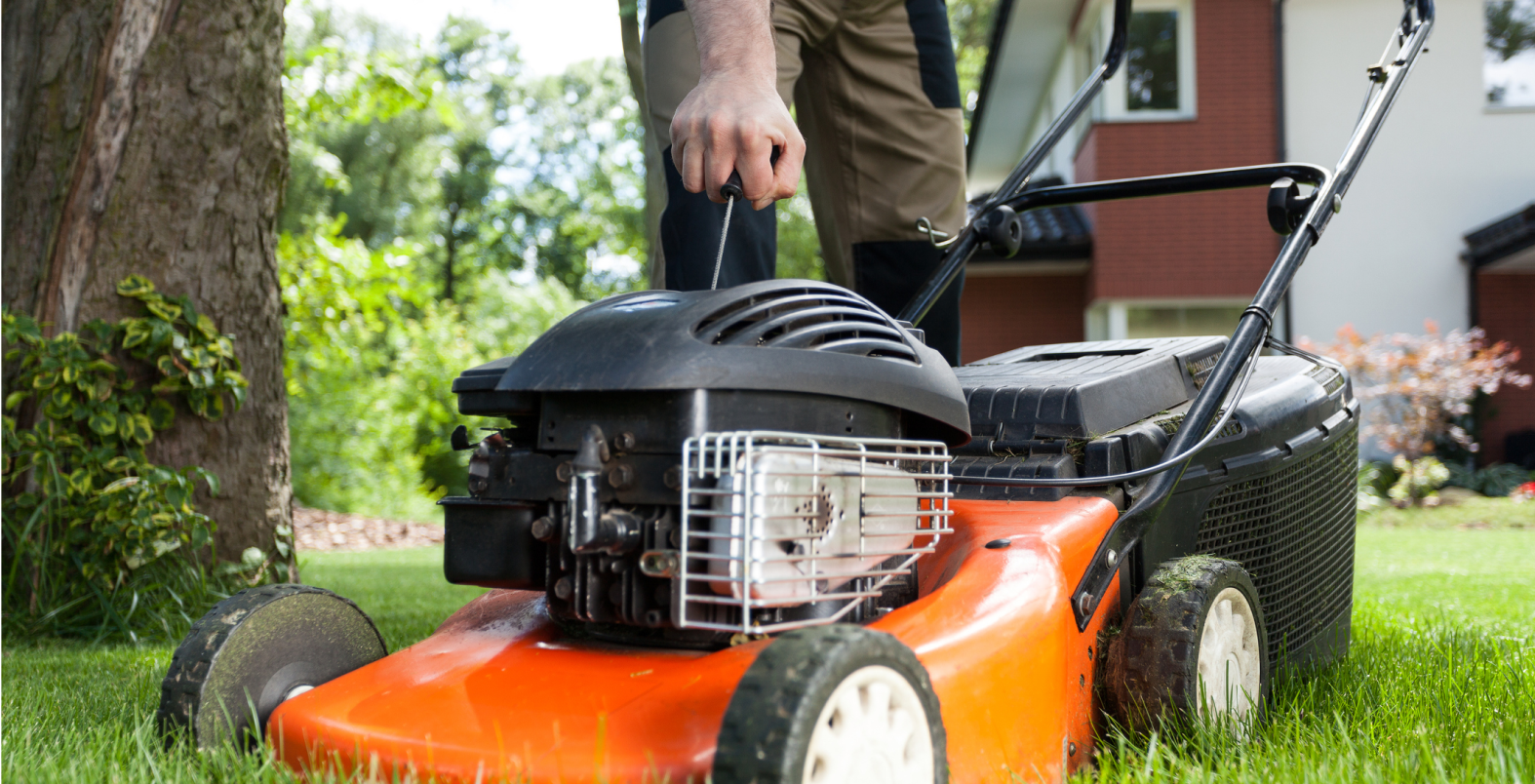 Person mowing lawn with orange lawnmower.